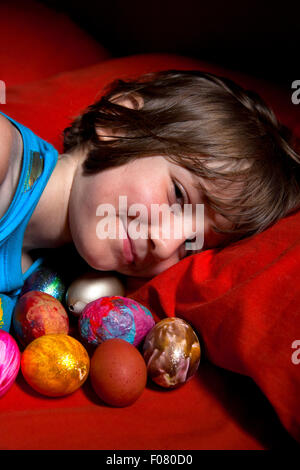 6 anno vecchio ragazzo disteso nel letto con la sua collezione di dipinti di uova. Foto Stock