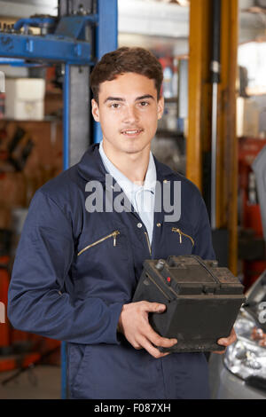 Apprendista meccanico azienda batteria auto nel negozio di riparazioni auto Foto Stock