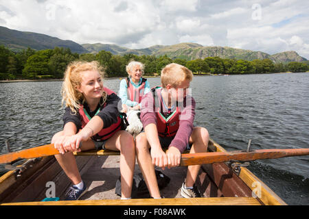 Una donna e due adolescenti in una barca a remi in Coniston Water nel distretto del lago, Cumbria, Regno Unito. Foto Stock