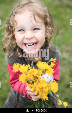 Happy Baby girl giocare all'aperto, carino bambino holding di fiori freschi Foto Stock