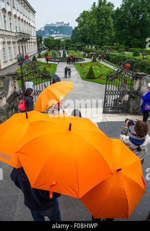 I turisti con ombrelloni arancione al palazzo e ai giardini di Mirabell a Salisburgo, Austria, in un giorno di pioggia. Foto Stock