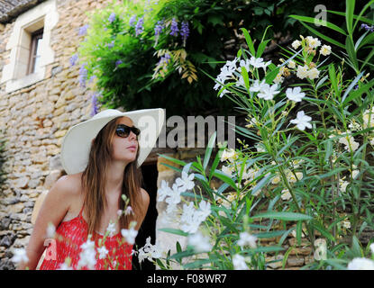 Giovane bella donna nel suo 20s indossando grande colmato cappello per il sole lo sniffing fiori fuori la sua vacanza gite Francia Foto Stock