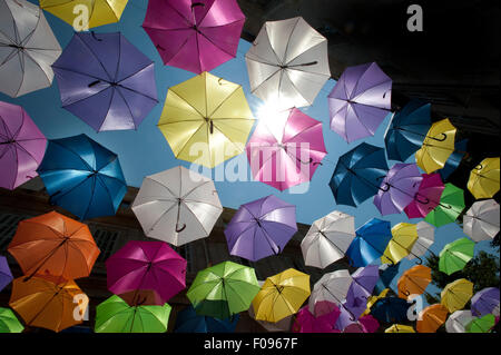 Vivacemente colorato floating ombrelloni riempire il cielo sopra la Rue Jean Jaures, Arles,Bouches-du-Rhône, Provenza, Francia Foto Stock