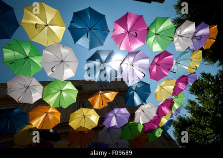 Vivacemente colorato floating ombrelloni riempire il cielo sopra la Rue Jean Jaures, Arles,Bouches-du-Rhône, Provenza, Francia Foto Stock