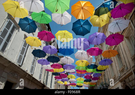 Vivacemente colorato floating ombrelloni riempire il cielo sopra la Rue Jean Jaures, Arles,Bouches-du-Rhône, Provenza, Francia Foto Stock