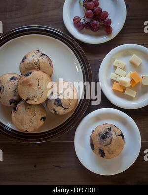 Diverse le piastre contenenti il muffin ai mirtilli, formaggio tagliato a cubetti e rosso uva senza semi di sedersi su un marrone da tavolo in legno. Foto Stock