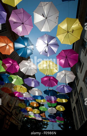 Vivacemente colorato floating ombrelloni riempire il cielo sopra la Rue Jean Jaures, Arles,Bouches-du-Rhône, Provenza, Francia Foto Stock