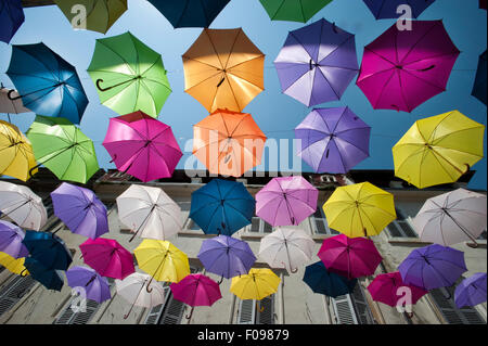 Vivacemente colorato floating ombrelloni riempire il cielo sopra la Rue Jean Jaures, Arles,Bouches-du-Rhône, Provenza, Francia Foto Stock