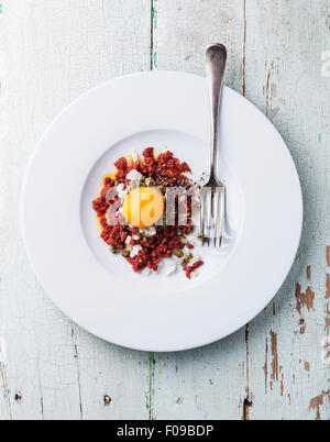 Tartare di carne di manzo con capperi e cipolla sulla piastra bianca su sfondo blu Foto Stock