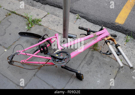 I resti di una bicicletta, ancora collegati da un cavo di sicurezza per un post, forlornly giace nel quartiere universitario di Pisa, Italia Foto Stock