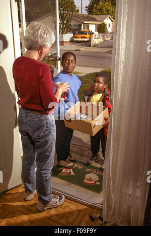 Volunteer African American boys raccogliere le donazioni di cibo in scatola per una carità locale da una donna senior di Long Beach, CA. Nota Santa Claus zerbino. Foto Stock