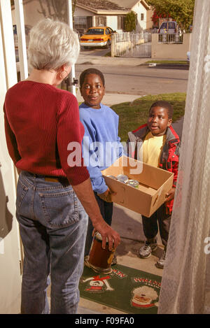 Volunteer African American boys raccogliere le donazioni di cibo in scatola per una carità locale da una donna senior di Long Beach, CA. Nota Santa Claus zerbino. Foto Stock