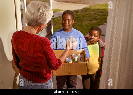 Volunteer African American boys raccogliere le donazioni di cibo in scatola per una carità locale da una donna senior di Long Beach, CA. Foto Stock