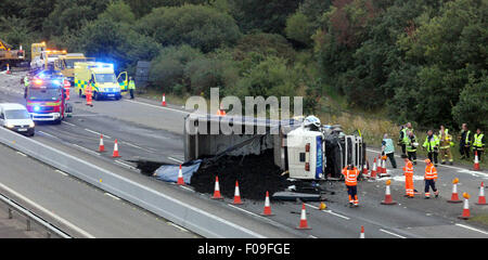 M3, Farnborough, Hampshire, Regno Unito. 10 Agosto, 2015. M3 vicino a Farnborough mostra GV della scena dopo un automezzo entra in collisione con una manutenzione autostrade veicolo parcheggiato sul disco spalla. Il carrello è stato dare protezione ai camion di recupero che stava recuperando un ripartiti automobilista. Il HGV dopo la alta velocità di collisione è venuto a poggiare sul suo lato dopo versando il suo carico su corsie uno e due del carrello principale modo. Due persone sono state portate in ospedale, uno da Air Ambulance la seconda da strada. Credito: Jason Kay/Alamy Live News Foto Stock