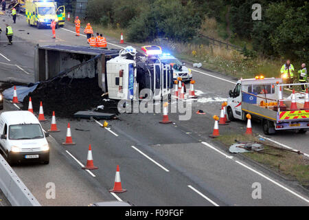 M3, Farnborough, Hampshire, Regno Unito. 10 Agosto, 2015. M3 vicino a Farnborough mostra GV della scena dopo un automezzo entra in collisione con una manutenzione autostrade veicolo parcheggiato sul disco spalla. Il carrello è stato dare protezione ai camion di recupero che stava recuperando un ripartiti automobilista. Il HGV dopo la alta velocità di collisione è venuto a poggiare sul suo lato dopo versando il suo carico su corsie uno e due del carrello principale modo. Due persone sono state portate in ospedale, uno da Air Ambulance la seconda da strada. Credito: Jason Kay/Alamy Live News Foto Stock