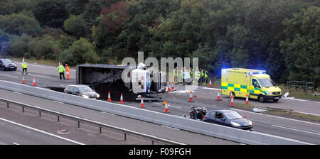 M3, Farnborough, Hampshire, Regno Unito. 10 Agosto, 2015. M3 vicino a Farnborough mostra GV della scena dopo un automezzo entra in collisione con una manutenzione autostrade veicolo parcheggiato sul disco spalla. Il carrello è stato dare protezione ai camion di recupero che stava recuperando un ripartiti automobilista. Il HGV dopo la alta velocità di collisione è venuto a poggiare sul suo lato dopo versando il suo carico su corsie uno e due del carrello principale modo. Due persone sono state portate in ospedale, uno da Air Ambulance la seconda da strada. Credito: Jason Kay/Alamy Live News Foto Stock