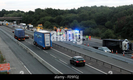 M3, Farnborough, Hampshire, Regno Unito. 10 Agosto, 2015. M3 vicino a Farnborough mostra GV della scena dopo un automezzo entra in collisione con una manutenzione autostrade veicolo parcheggiato sul disco spalla. Il carrello è stato dare protezione ai camion di recupero che stava recuperando un ripartiti automobilista. Il HGV dopo la alta velocità di collisione è venuto a poggiare sul suo lato dopo versando il suo carico su corsie uno e due del carrello principale modo. Due persone sono state portate in ospedale, uno da Air Ambulance la seconda da strada. Credito: Jason Kay/Alamy Live News Foto Stock