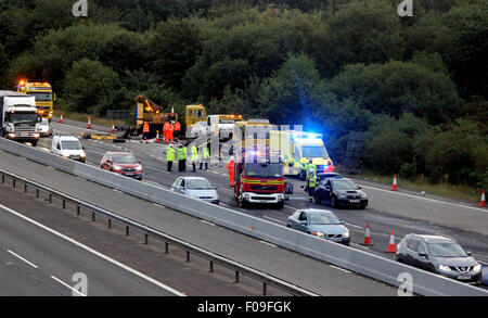 M3, Farnborough, Hampshire, Regno Unito. 10 Agosto, 2015. M3 vicino a Farnborough mostra GV della scena dopo un automezzo entra in collisione con una manutenzione autostrade veicolo parcheggiato sul disco spalla. Il carrello è stato dare protezione ai camion di recupero che stava recuperando un ripartiti automobilista. Il HGV dopo la alta velocità di collisione è venuto a poggiare sul suo lato dopo versando il suo carico su corsie uno e due del carrello principale modo. Due persone sono state portate in ospedale, uno da Air Ambulance la seconda da strada. Credito: Jason Kay/Alamy Live News Foto Stock