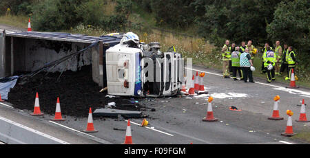 M3, Farnborough, Hampshire, Regno Unito. 10 Agosto, 2015. M3 vicino a Farnborough mostra GV della scena dopo un automezzo entra in collisione con una manutenzione autostrade veicolo parcheggiato sul disco spalla. Il carrello è stato dare protezione ai camion di recupero che stava recuperando un ripartiti automobilista. Il HGV dopo la alta velocità di collisione è venuto a poggiare sul suo lato dopo versando il suo carico su corsie uno e due del carrello principale modo. Due persone sono state portate in ospedale, uno da Air Ambulance la seconda da strada. Credito: Jason Kay/Alamy Live News Foto Stock