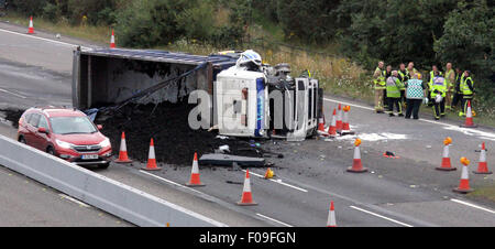 M3, Farnborough, Hampshire, Regno Unito. 10 Agosto, 2015. M3 vicino a Farnborough mostra GV della scena dopo un automezzo entra in collisione con una manutenzione autostrade veicolo parcheggiato sul disco spalla. Il carrello è stato dare protezione ai camion di recupero che stava recuperando un ripartiti automobilista. Il HGV dopo la alta velocità di collisione è venuto a poggiare sul suo lato dopo versando il suo carico su corsie uno e due del carrello principale modo. Due persone sono state portate in ospedale, uno da Air Ambulance la seconda da strada. Credito: Jason Kay/Alamy Live News Foto Stock