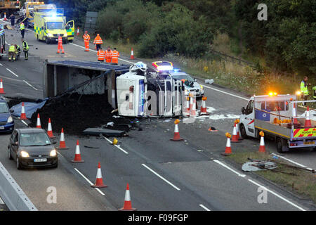 M3, Farnborough, Hampshire, Regno Unito. 10 Agosto, 2015. M3 vicino a Farnborough mostra GV della scena dopo un automezzo entra in collisione con una manutenzione autostrade veicolo parcheggiato sul disco spalla. Il carrello è stato dare protezione ai camion di recupero che stava recuperando un ripartiti automobilista. Il HGV dopo la alta velocità di collisione è venuto a poggiare sul suo lato dopo versando il suo carico su corsie uno e due del carrello principale modo. Due persone sono state portate in ospedale, uno da Air Ambulance la seconda da strada. Credito: Jason Kay/Alamy Live News Foto Stock