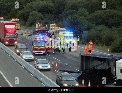 M3, Farnborough, Hampshire, Regno Unito. 10 Agosto, 2015. M3 vicino a Farnborough mostra GV della scena dopo un automezzo entra in collisione con una manutenzione autostrade veicolo parcheggiato sul disco spalla. Il carrello è stato dare protezione ai camion di recupero che stava recuperando un ripartiti automobilista. Il HGV dopo la alta velocità di collisione è venuto a poggiare sul suo lato dopo versando il suo carico su corsie uno e due del carrello principale modo. Due persone sono state portate in ospedale, uno da Air Ambulance la seconda da strada. Credito: Jason Kay/Alamy Live News Foto Stock