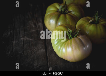 Verde grande immaturo RAF pomodori su un vecchio tavolo di legno. Scuro in stile rustico. La luce naturale del giorno. Con copia spazio sulla sinistra Foto Stock