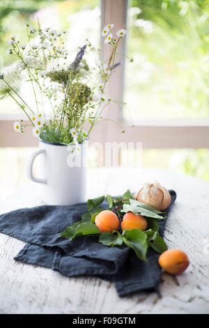 Le albicocche e le cipolle con il grigio asciugatutto e bouquet di fiori di colore bianco sul tavolo di legno con vista giardino in background Foto Stock