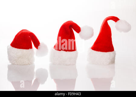 Tre cappelli Santa in una fila per il Natale. Isolato su sfondo bianco con la riflessione. Spazio per testo, copiare lo spazio. Foto Stock