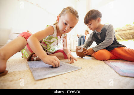 Piccolo Ragazzo e ragazza foto di colorazione con chalk colori mentre la seduta sul pavimento nel soggiorno di casa. Foto Stock