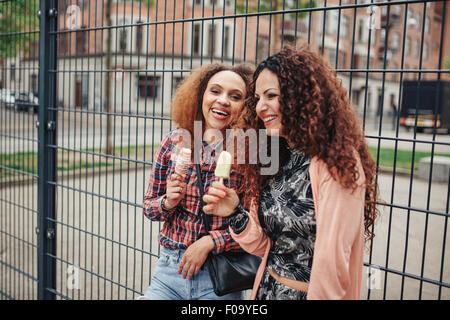 Felici donne mangiare un gelato all'esterno. Ragazza amici divertendosi sulla strada della citta'. Foto Stock