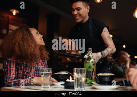 Donna che parla al cameriere al ristorante. Giovane donna seduta al cafe con cameriere in piedi dalla sorridente. Foto Stock