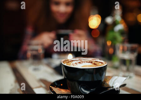 Immagine ravvicinata di tazza di caffè sul tavolo al ristorante, con una donna seduta in background. Focus sulla tazza di caffè.