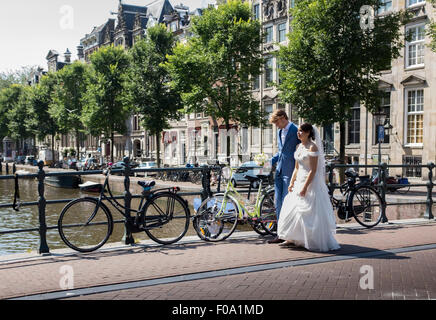 Gli sposi a piedi attraverso un ponte sul canale di Amsterdam dopo la loro cerimonia di nozze Foto Stock