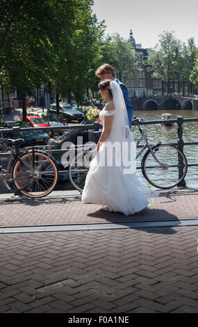 Gli sposi a piedi attraverso un ponte sul canale di Amsterdam dopo la loro cerimonia di nozze Foto Stock
