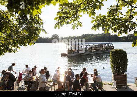 La gente seduta a Maschseefest giardino della birra con il traghetto a sfondo, Hannover, Germania Foto Stock