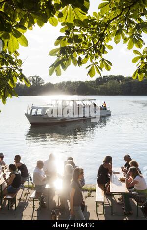 La gente seduta a Maschseefest giardino della birra con il traghetto a sfondo, Hannover, Germania Foto Stock