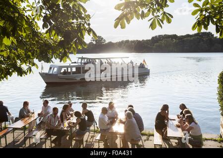 La gente seduta a Maschseefest giardino della birra con il traghetto a sfondo, Hannover, Germania Foto Stock