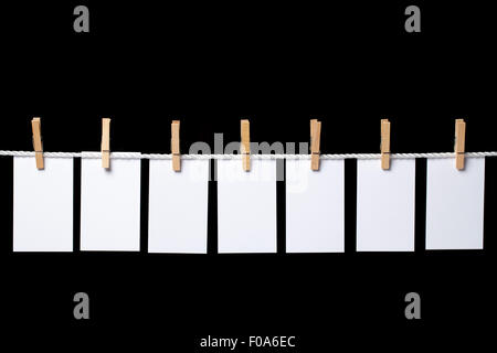 Immagine di sette piccoli fogli di carta bianca appeso con clothespins sulla fune. La composizione è isolato su sfondo nero. La rela Foto Stock