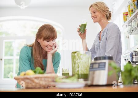 Le donne di bere verde frullato vegano in cucina Foto Stock