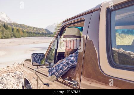 Metà uomo adulto seduto nel carrello, sporgersi finestra, guardando la fotocamera Foto Stock