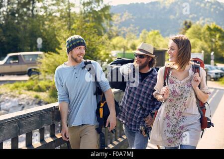 Tre persone che camminano insieme trasportano zaini, sorridente Foto Stock