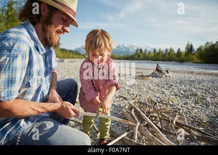 Metà uomo adulto e bambino utilizzando pocket coltello per togliere la corteccia dal ramo, Wallgau, Baviera, Germania Foto Stock