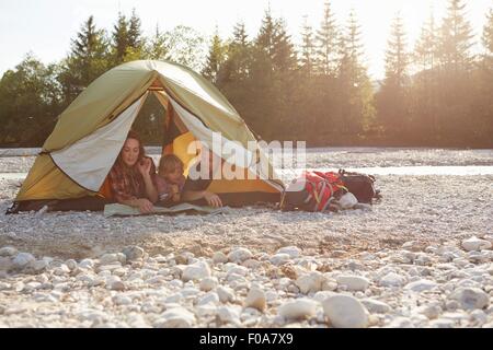 Famiglia giacente su fronti fianco a fianco in tenda decompressi, guardando alla mappa Foto Stock