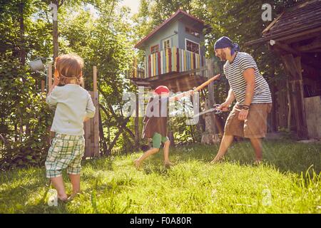 Padre e i due figli in giardino, indossando costumi, giocando con finta di spade Foto Stock