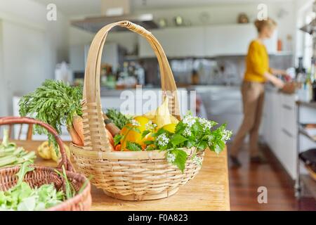 Orto in cesti sulla tavola in cucina, donna matura lavorando in background Foto Stock