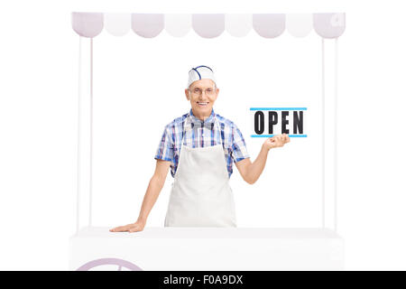 Studio shot di un senior vendor tenendo un segno aperto e in posa dietro un supporto isolato su sfondo bianco Foto Stock