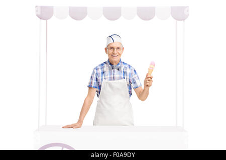 Studio shot di un gelato venditore di trattenimento di un cono gelato e in posa dietro uno stallo isolati su sfondo bianco Foto Stock