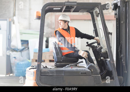 Giovane maschio lavoratore magazzino inversione di carrello elevatore a forche in magazzino Foto Stock