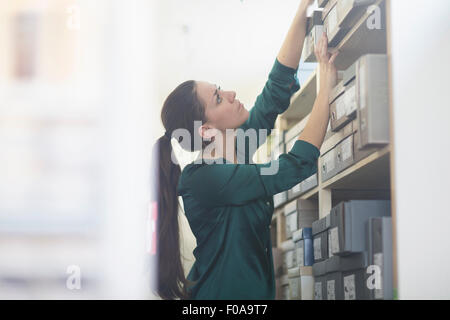 Femmina assistente vendite raggiungendo per scatola di scarpe in negozio di scarpe e magazzini Foto Stock